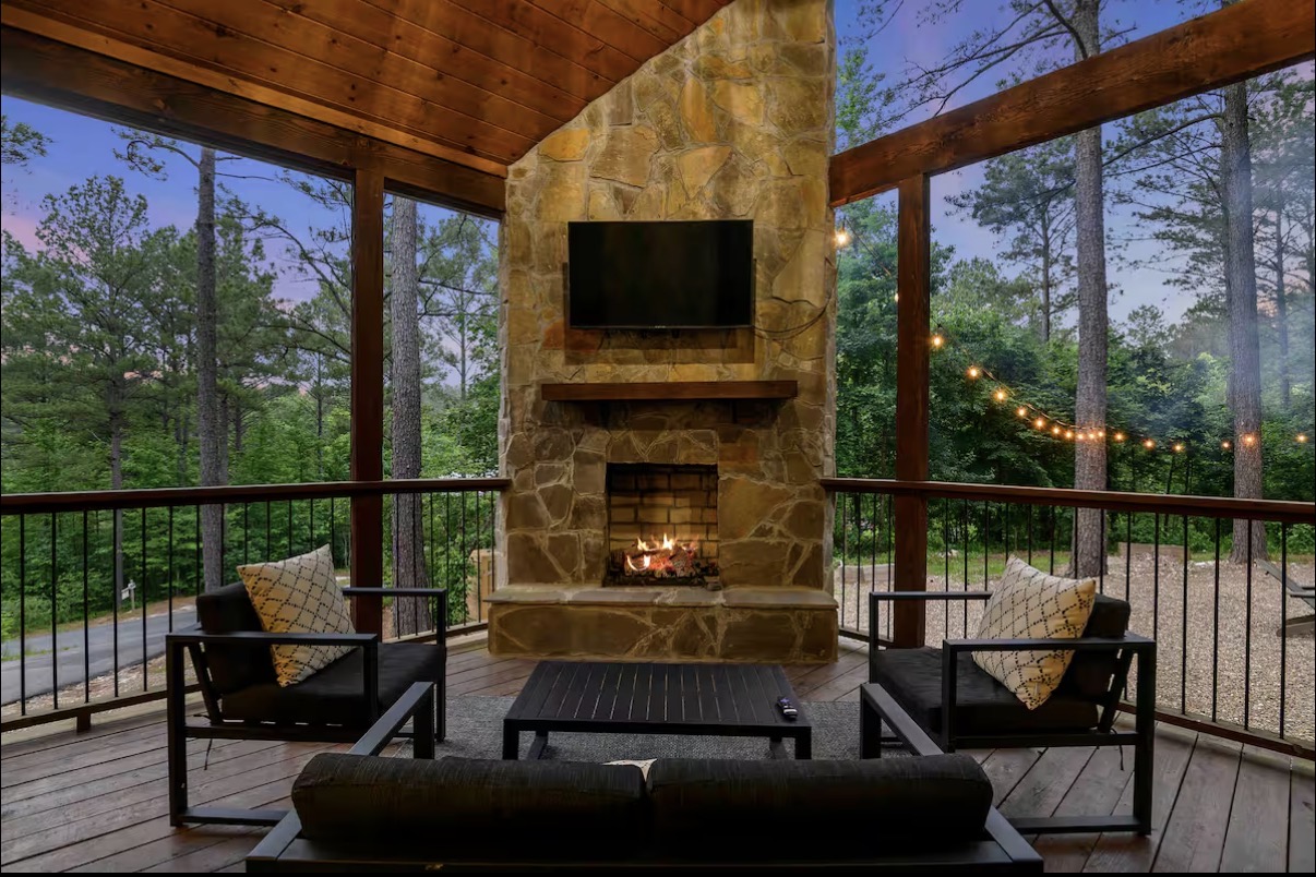 Sound of Sunshine — screened deck with stone fireplace, mounted TV and string lights at dusk